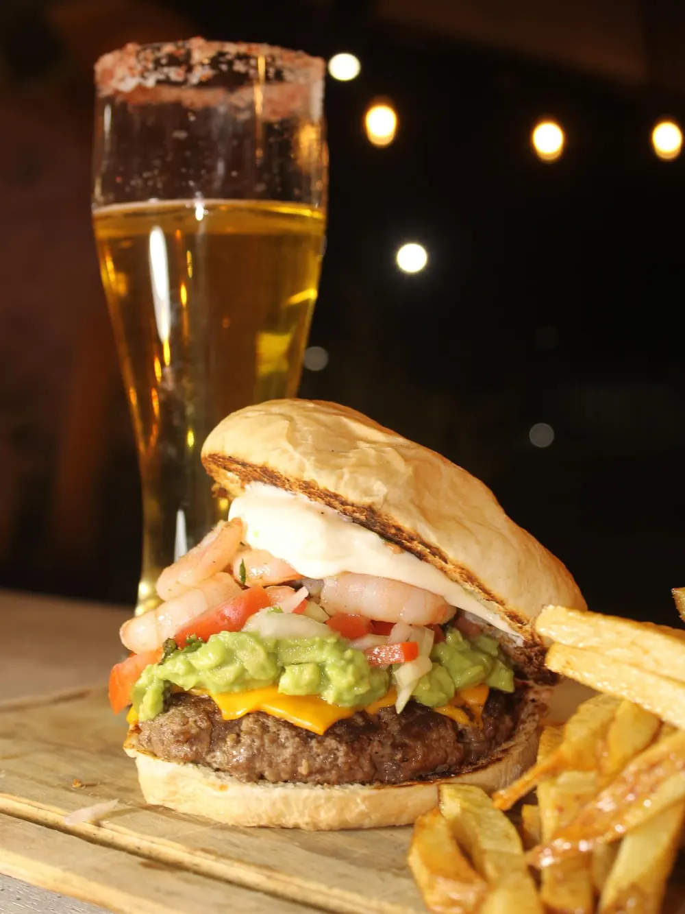 Hamburguesa con guacamole y camarones junto a papas fritas